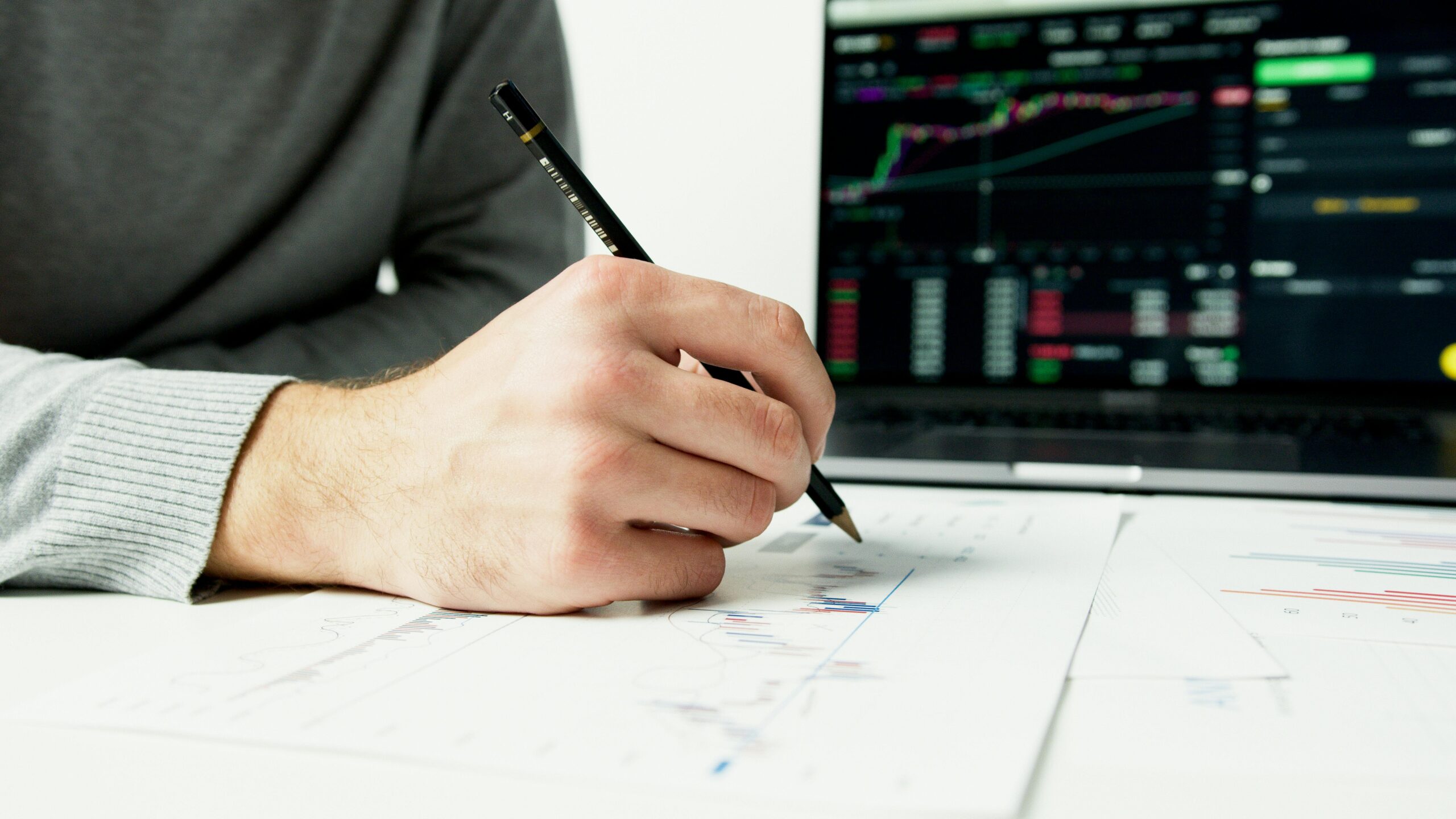 Close-up of a person analyzing financial charts with a laptop displaying stock market data.
