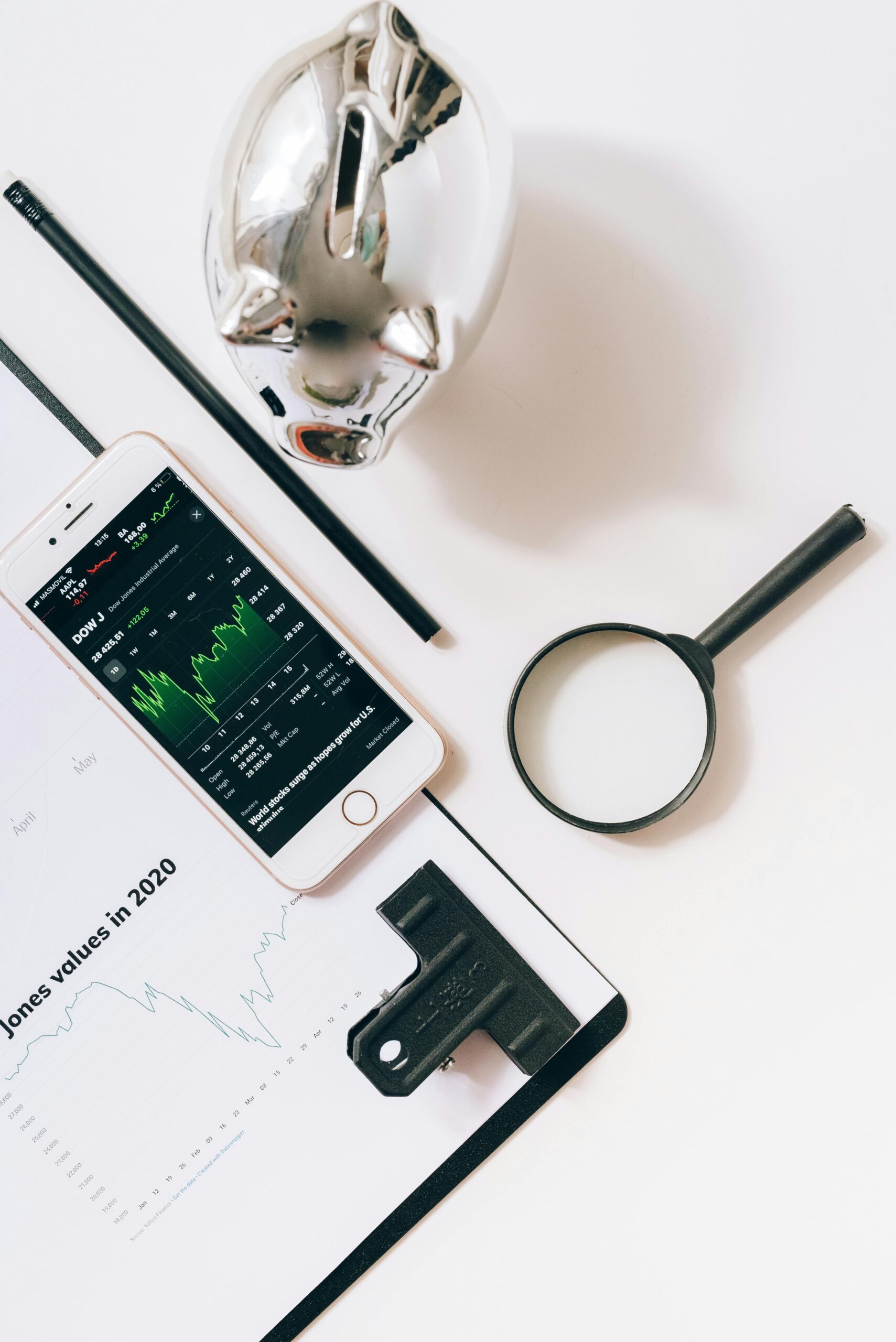 Flat lay of financial tools including smartphone, magnifying glass, and stock data for business insights.