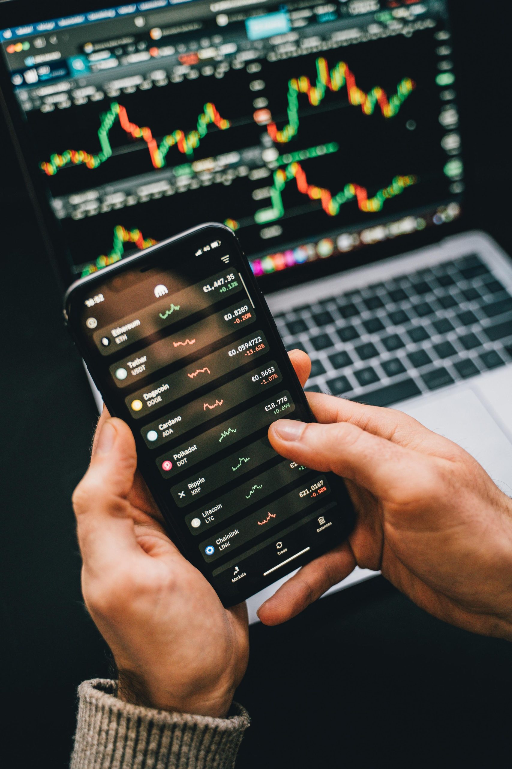 Hands holding smartphone with stock app, laptop displaying charts. Perfect for financial and technology themes.