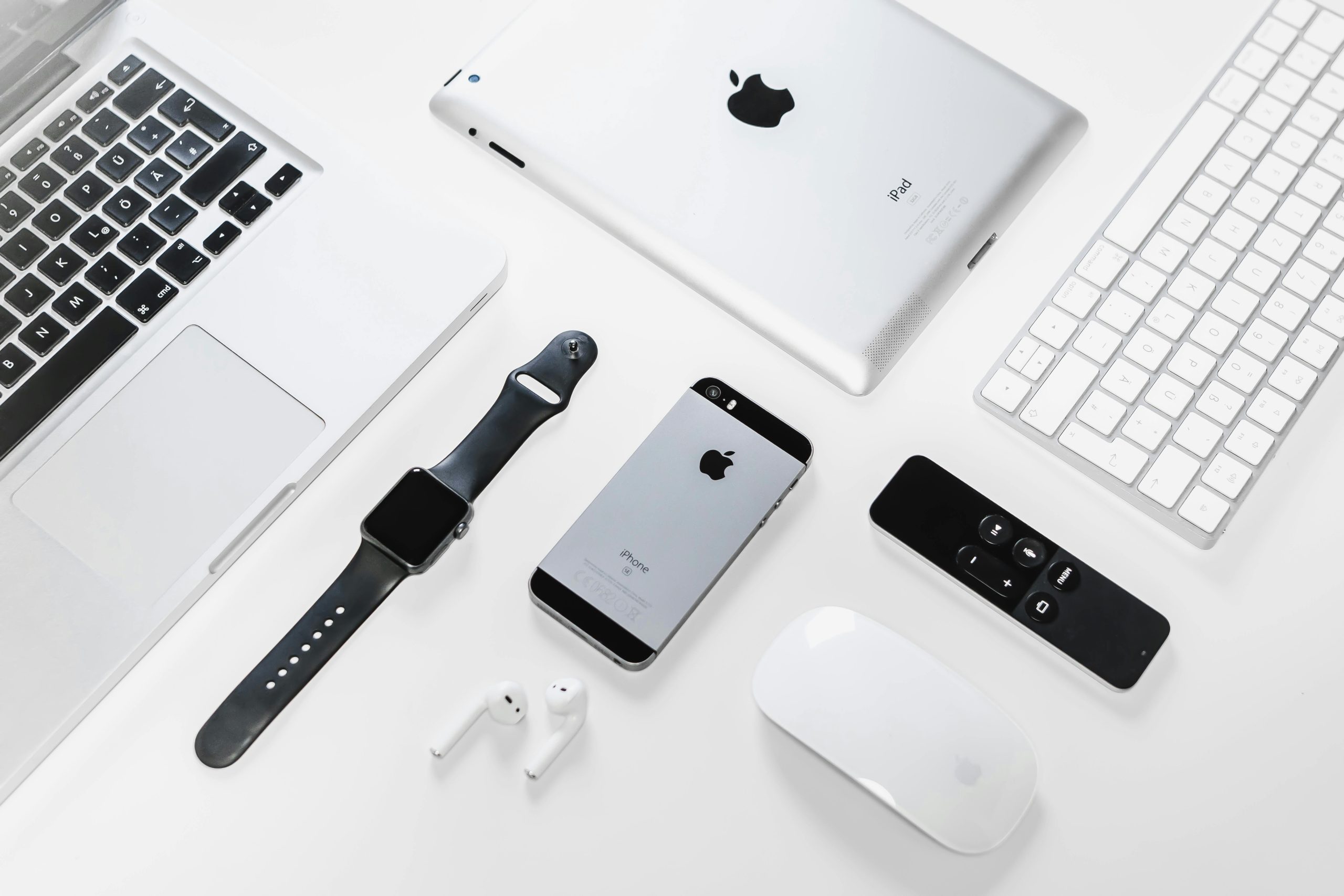 Flat lay of Apple devices including iPhone, iPad, MacBook, and Watch on a white surface, ideal for tech enthusiasts.
